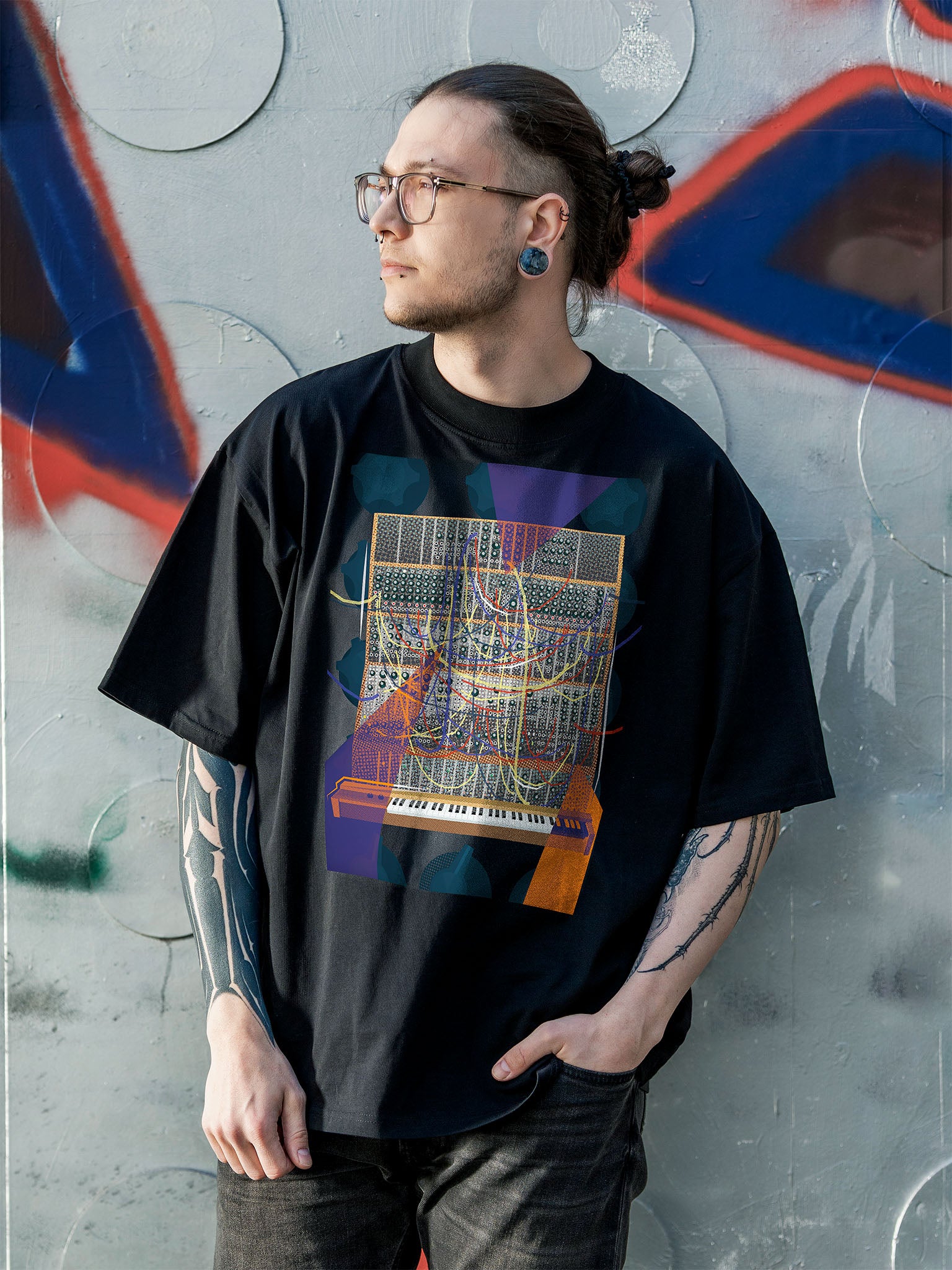 Black T-shirt with a vibrant graphic design of a modular synthesizer with patch cables and knobs on the background with orange and purple geometric colorful elements.