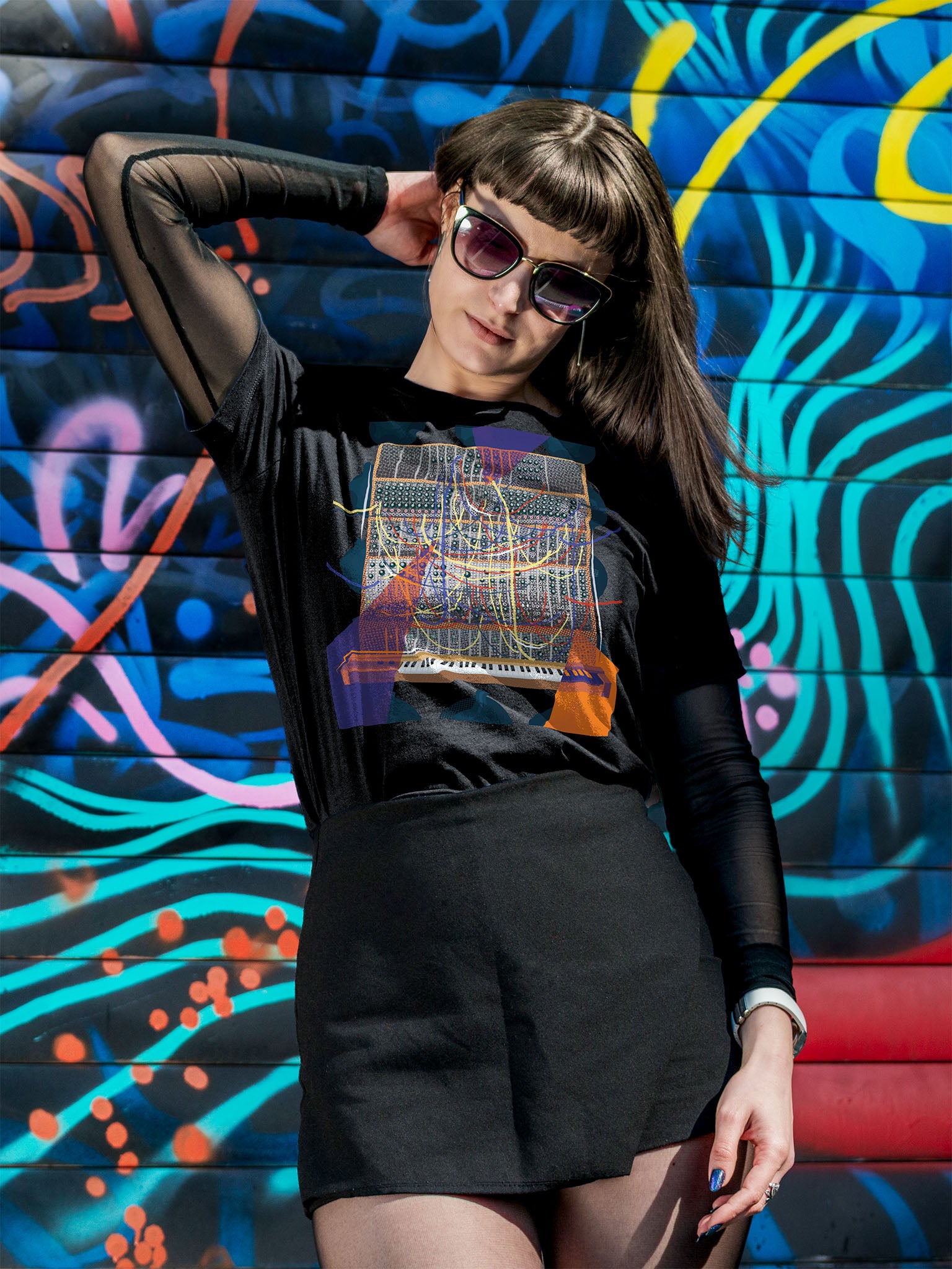 Black T-shirt with a vibrant graphic design of a modular synthesizer with patch cables and knobs on the background with orange and purple geometric colorful elements.