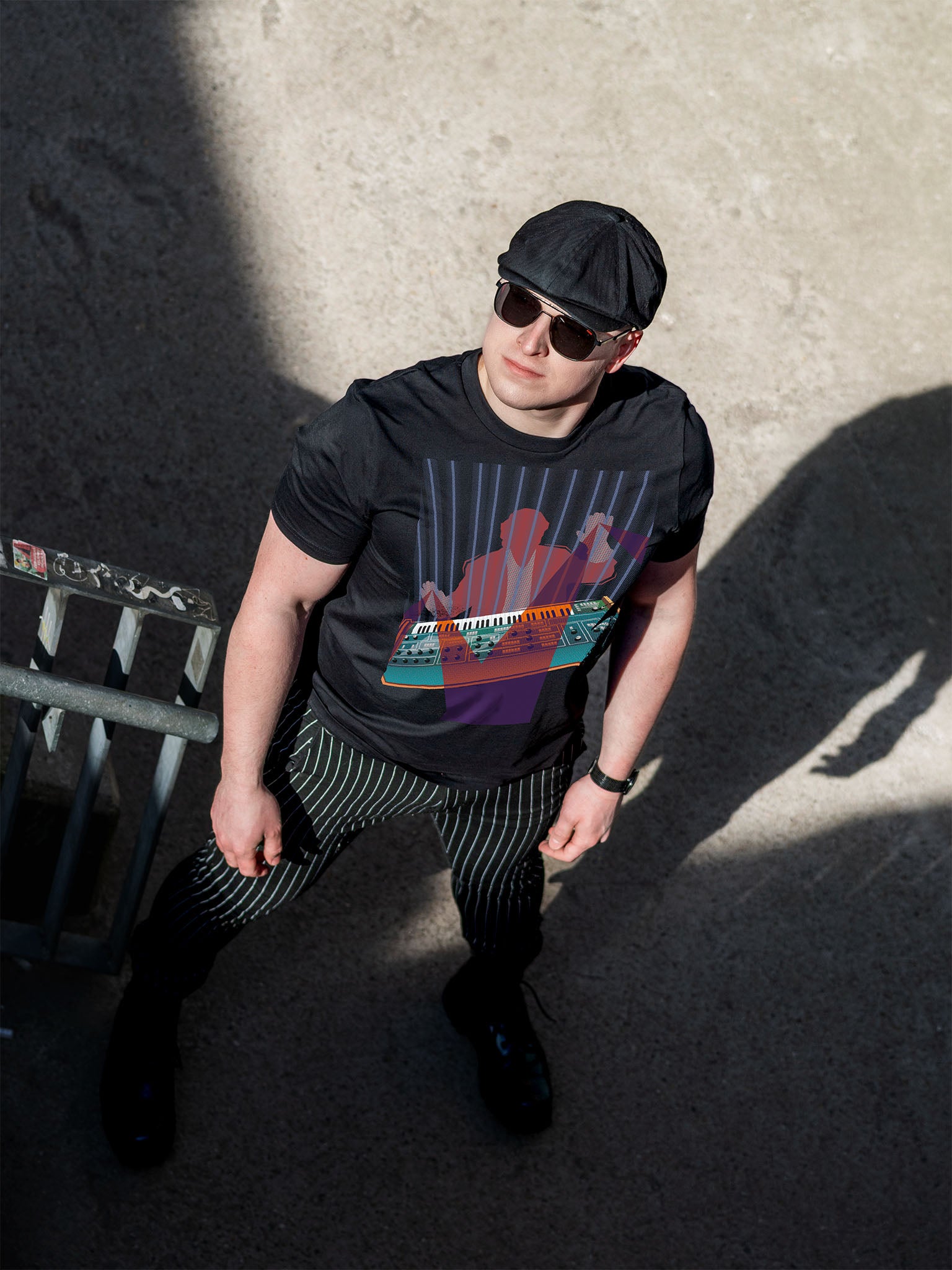 Black T-shirt with a colorful design of a man playing on a synthesizer and purple light beams go out of his hands.