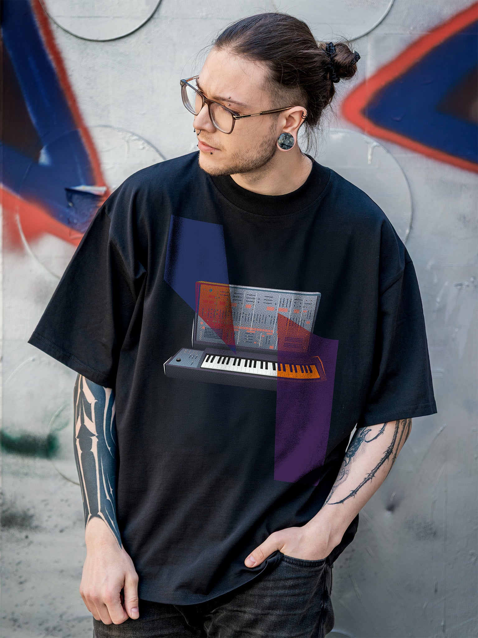 Black t-shirt with a graphic design of a keyboard and colorful abstract geometric elements against a graffiti-covered wall.